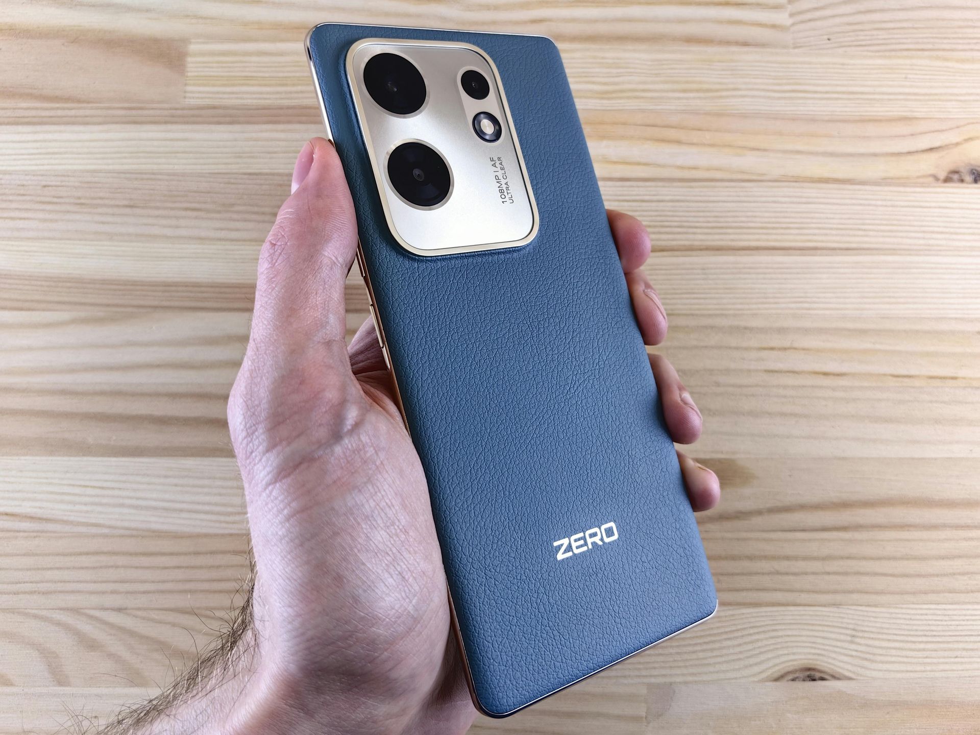 A hand holds a blue textured smartphone with a large gold camera housing and