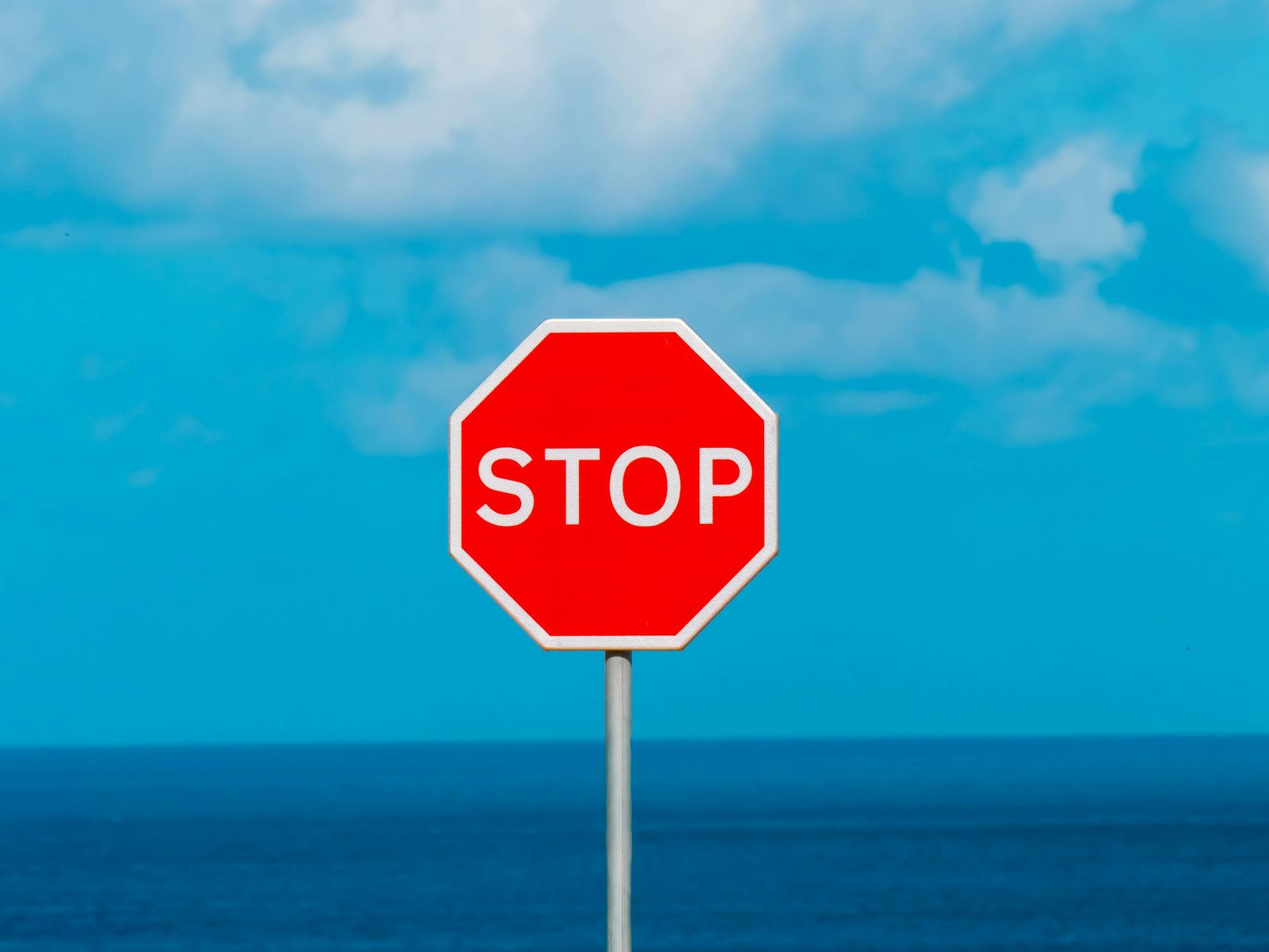 Red stop sign against a blue sky, above a body of water.