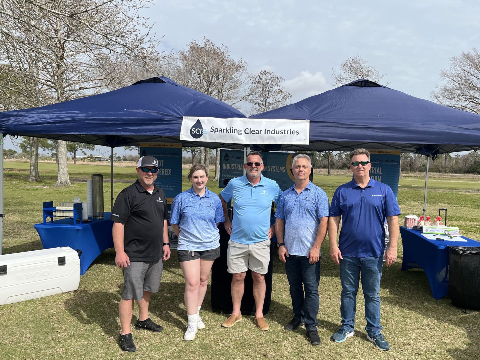 A group of people are standing in front of a tent on a golf course with a sign that says Sparkling Clear Industries.