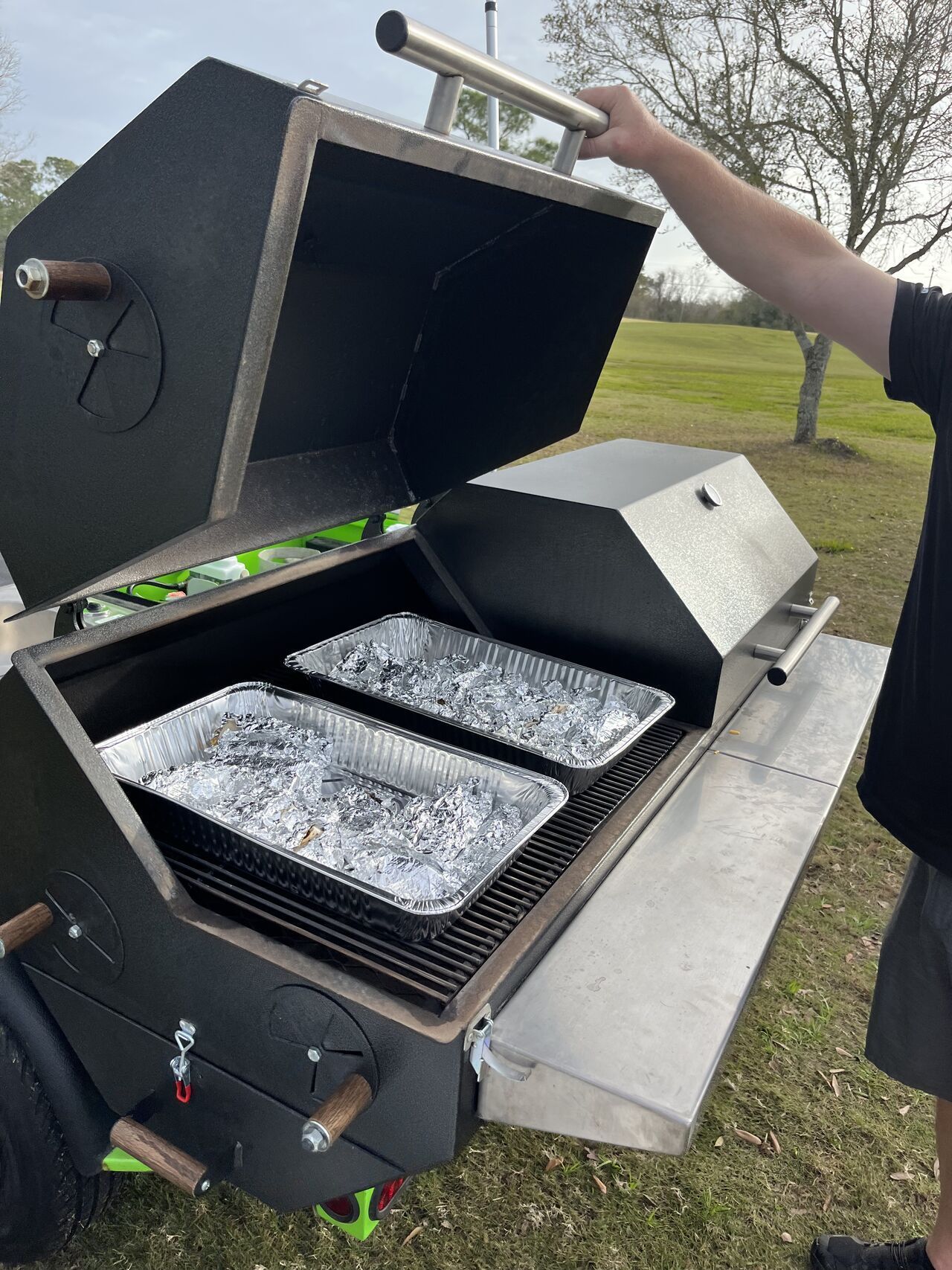 A man is standing in front of a grill with the lid open.
