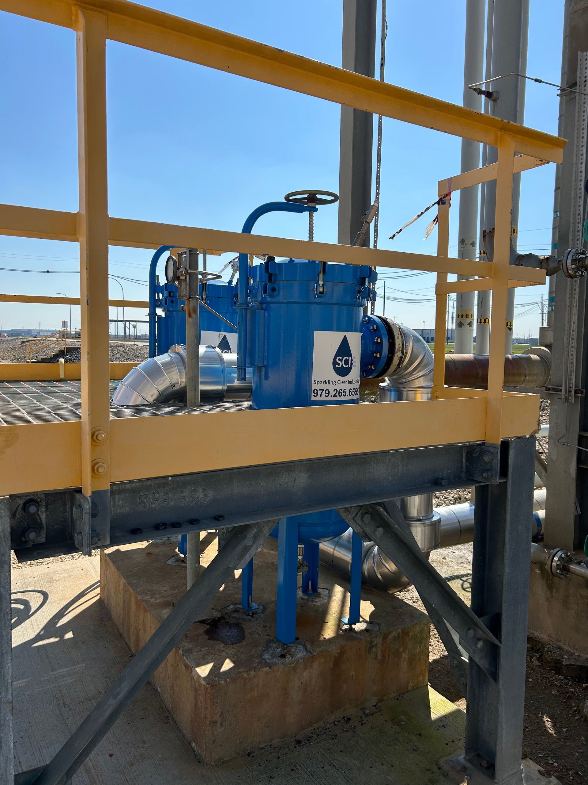 A yellow railing surrounds a blue filter housing from Sparkling Clear Industries with a hose attached to it