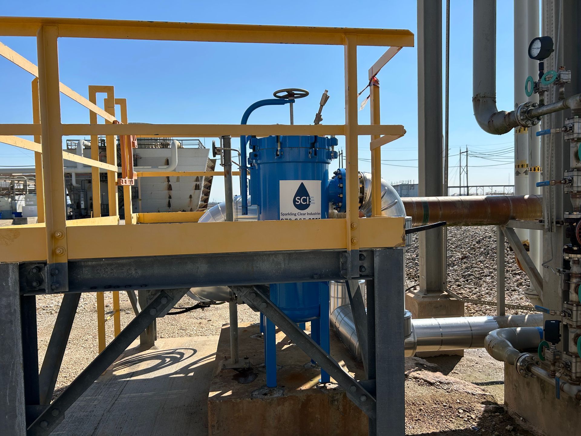 A blue filter housing from Sparkling Clear Industries is sitting on top of a metal platform with a yellow railing.