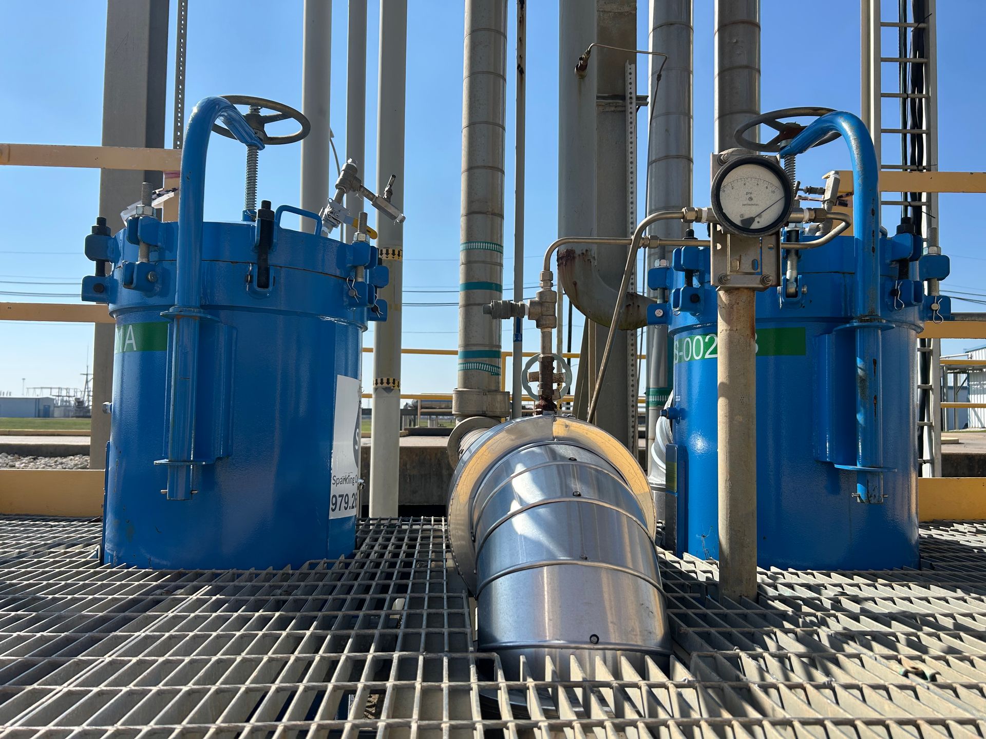 A couple of blue filter housing from Sparkling Clear Industries are sitting on top of a metal platform.