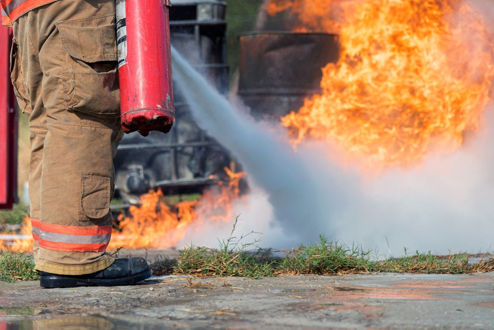 Firefighter spraying water on a blaze with a hose, flames visible in the background.
