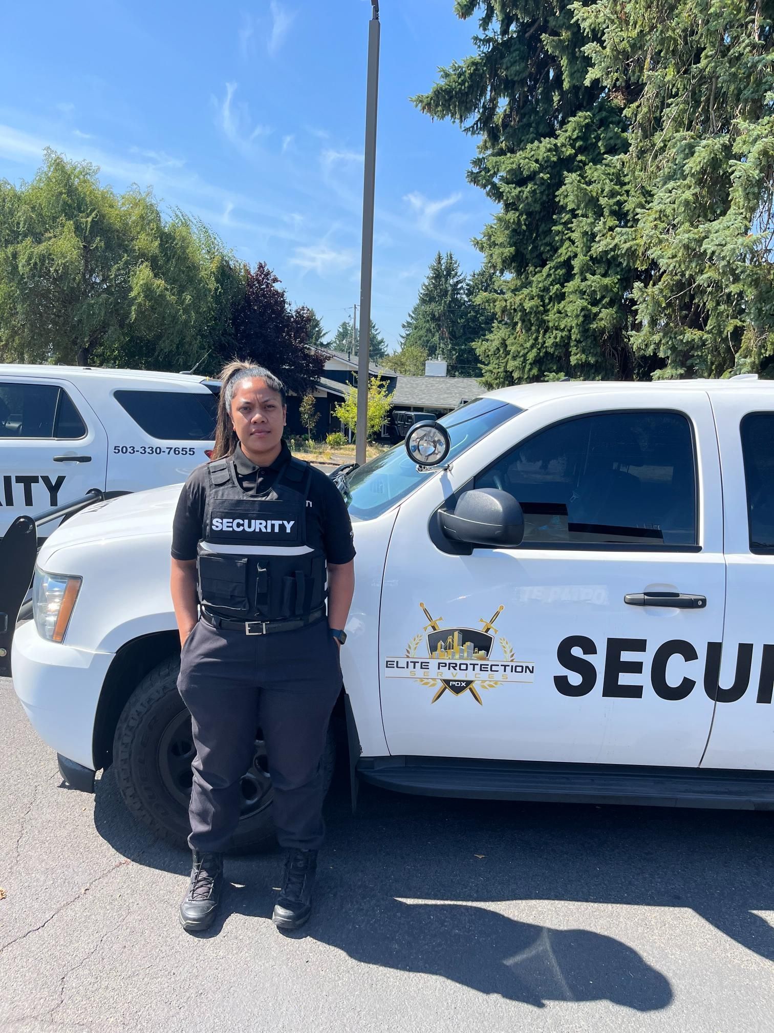 Security guard standing beside a white security vehicle on a sunny street