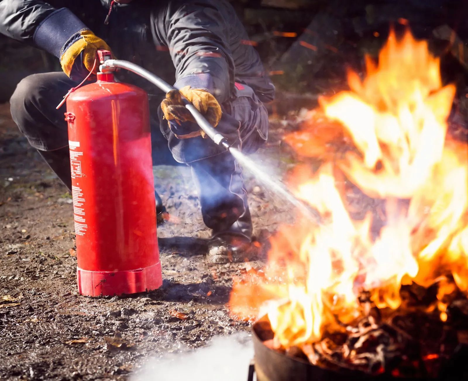 Person using a fire extinguisher to put out a large outdoor fire on gravel.