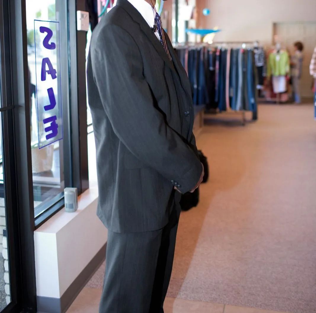 A man in a dark suit stands by a shop window in a clothing store.