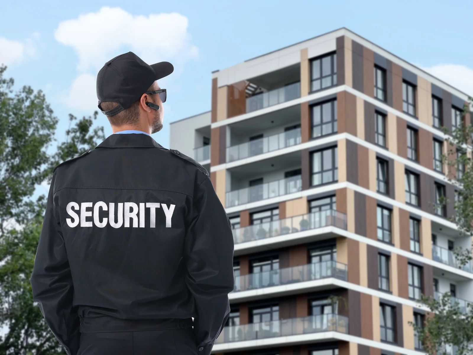 Security guard standing outside a modern apartment building, seen from behind.
