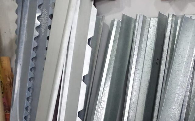 Láminas de metal corrugado apiladas en color plata y gris, apoyadas verticalmente contra una pared.
