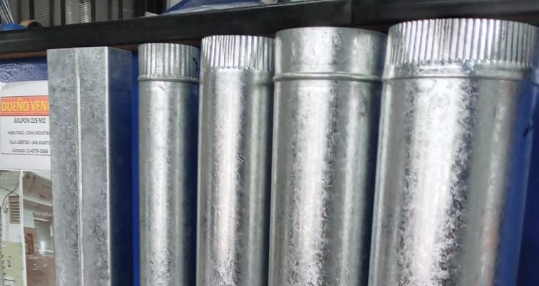 Una hilera de conductos de ventilación de metal brillante y un tubo azul almacenados en posición vertical.