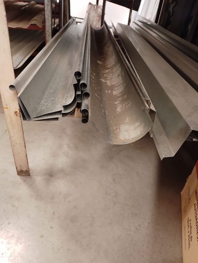 Paneles y molduras metálicas para techos apilados en un pasillo de un taller sobre un suelo de hormigón.