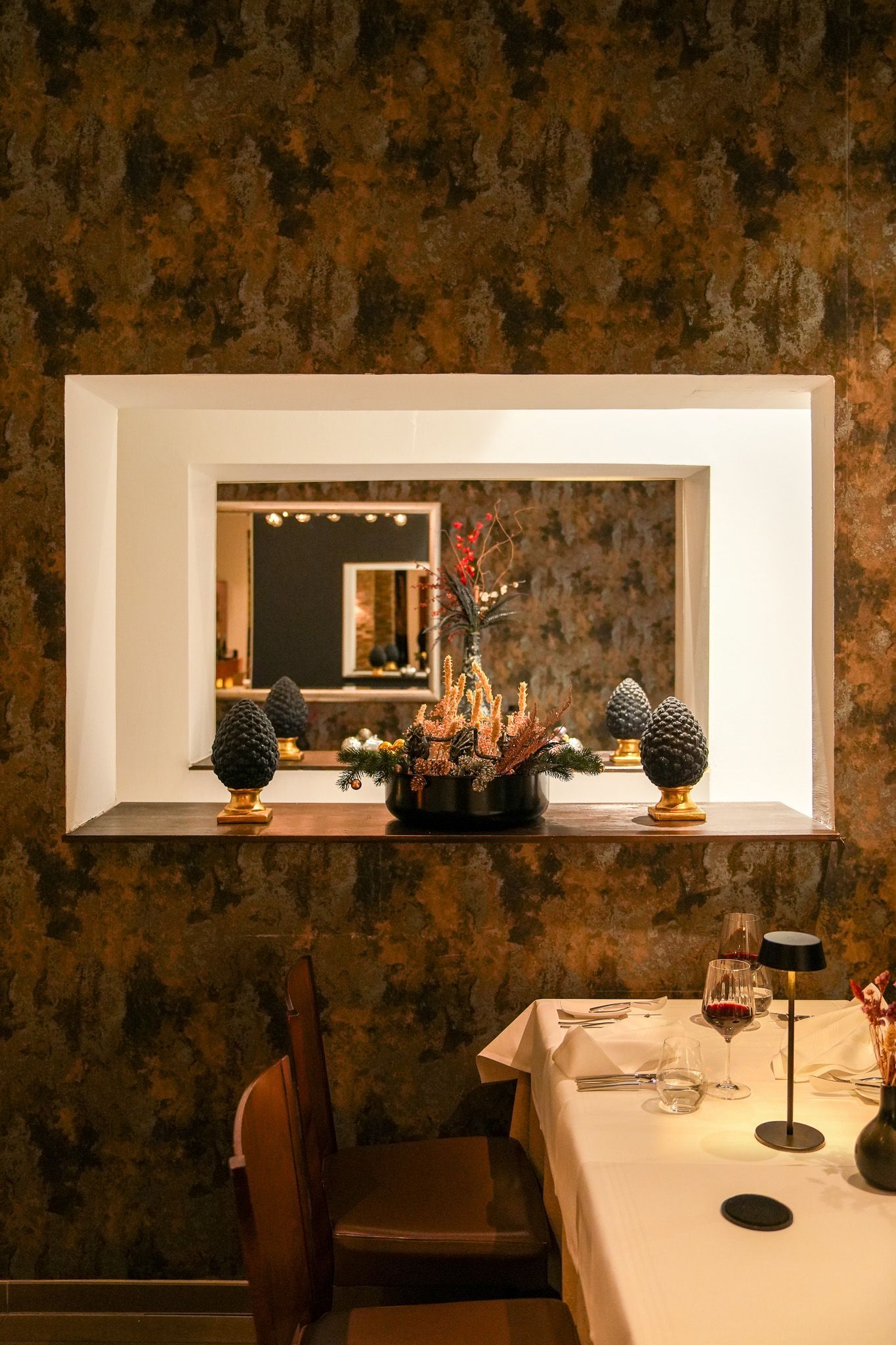 Restaurantinterieur mit einem zum Essen gedeckten Tisch, einer dekorativen Nische mit Ornamenten und einer gemusterten Wand.