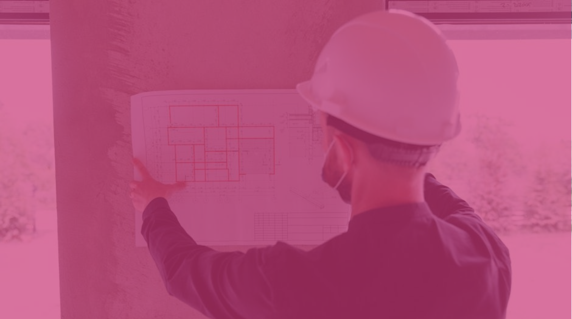Worker in a hard hat reviews a blueprint on a wall at a construction site.