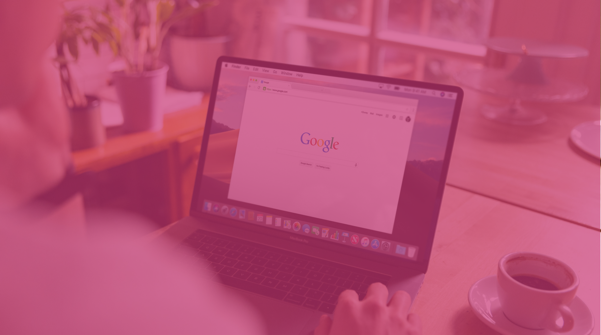 Person using a laptop at a desk with a coffee cup nearby, viewed through a pink-tinted blur.