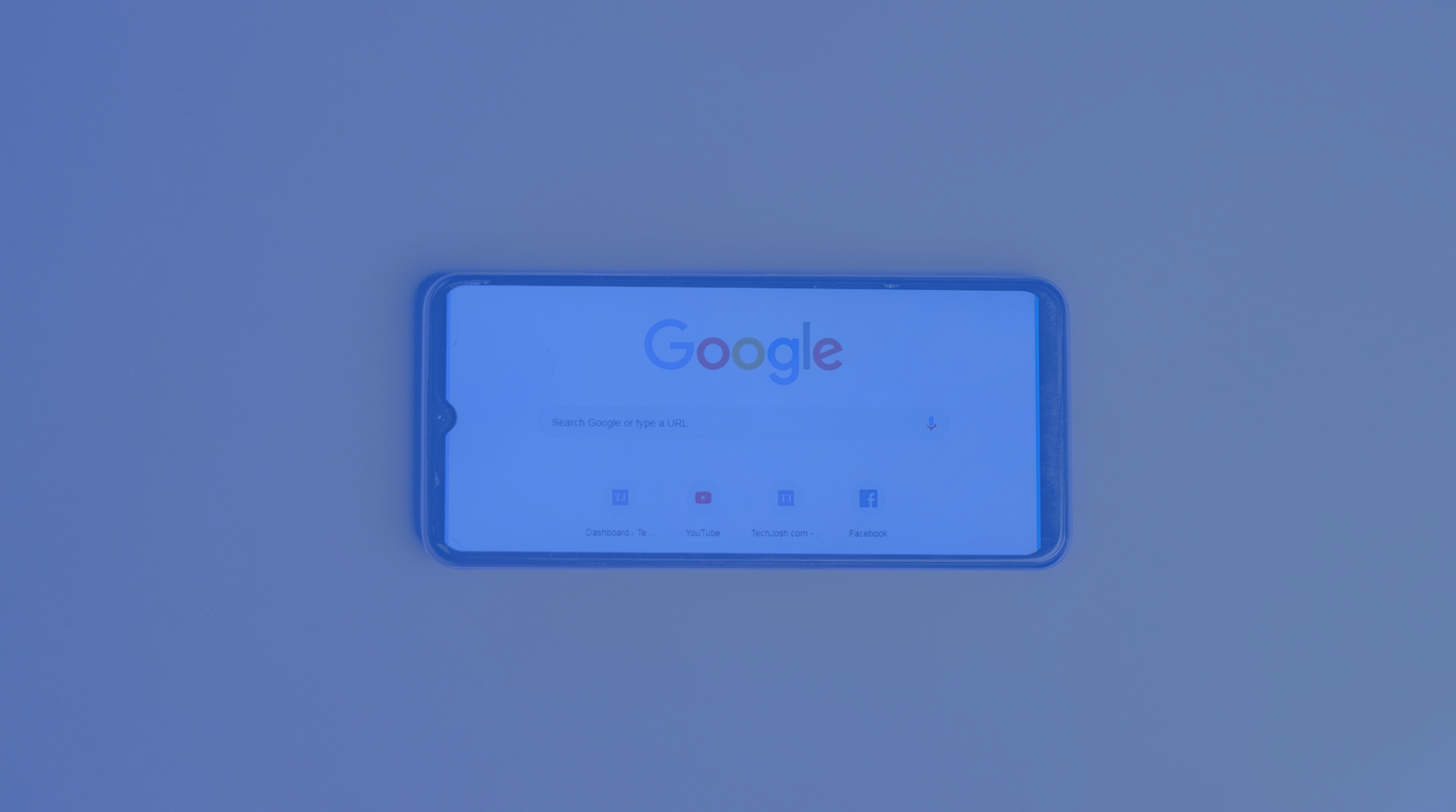 A smartphone on a blue surface showing the Google homepage.