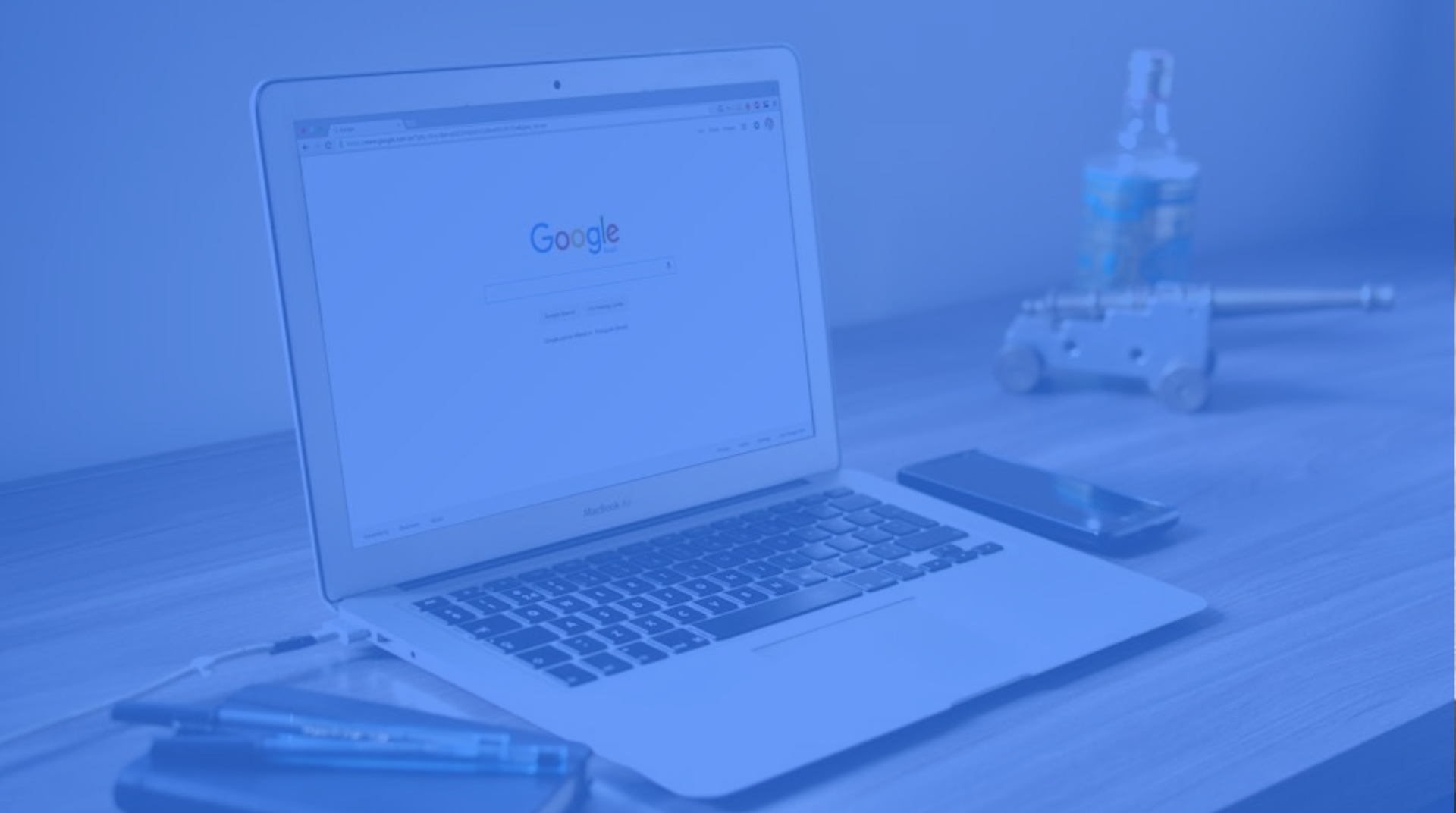 Blue-tinted laptop on a desk with a Google search page, notebook, and water bottle in the background
