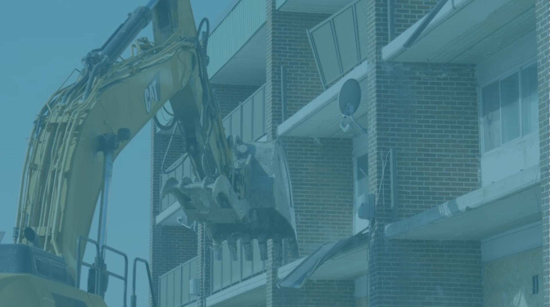Excavator demolishing a brick building facade beside apartment balconies
