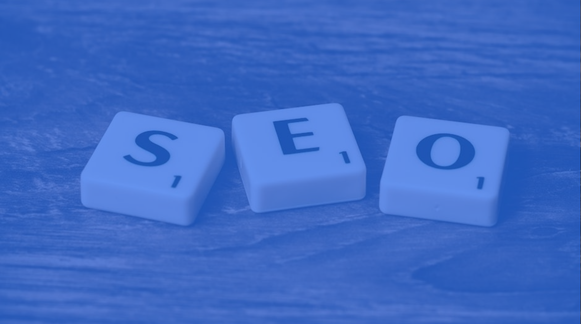 Three white letter tiles spelling “SEO” on a blue surface.