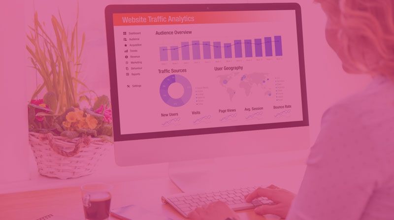 Person viewing a pink-tinted analytics dashboard on a desktop monitor in an office workspace