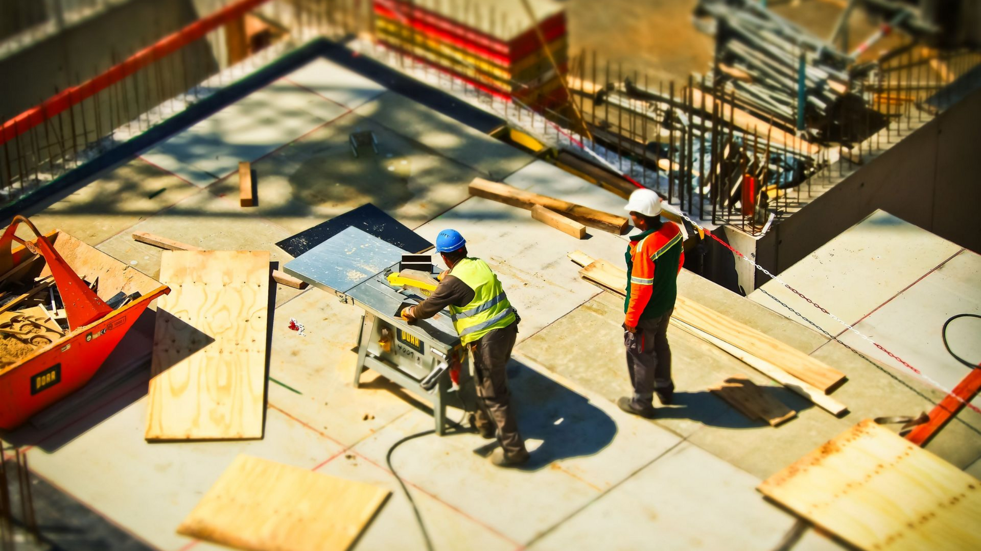 Construction workers measuring plywood on a building site with tools and lumber scattered nearby