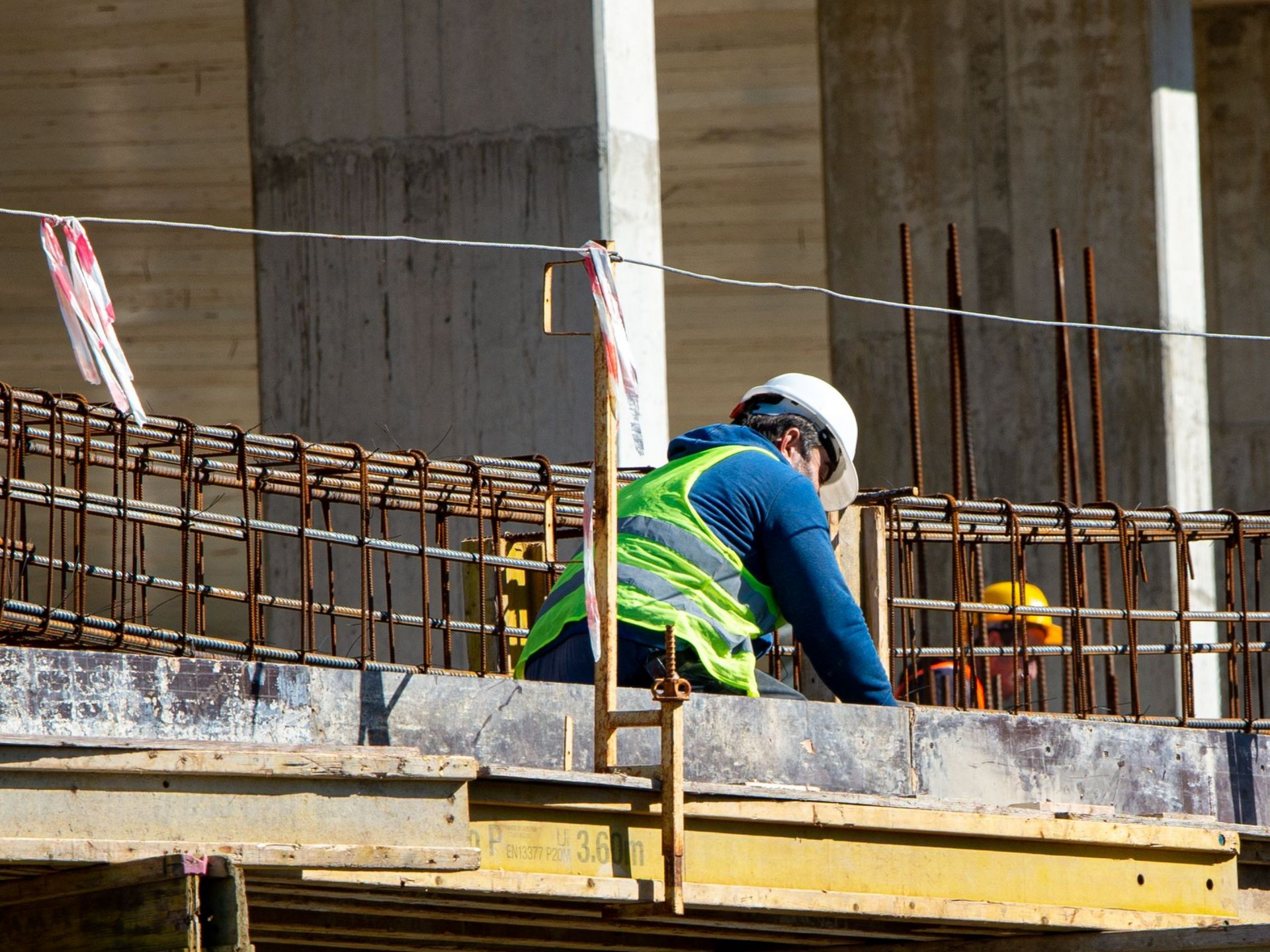 Construction worker in a neon vest and hard hat working on rebar at a concrete building site