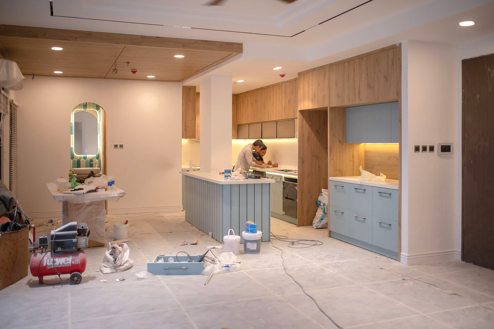 Renovation site with three windows, peeling walls, ladder, mop, and scattered tools on a bare floor