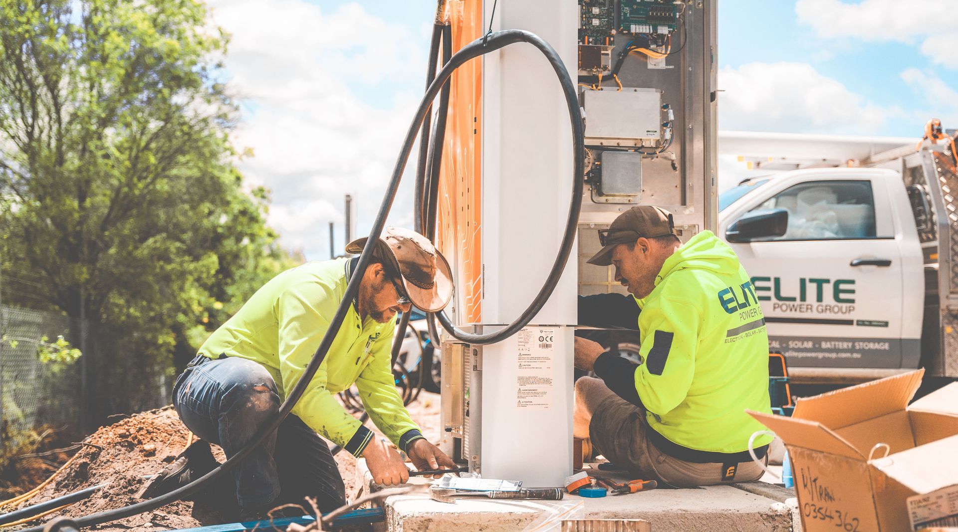 Two workers in neon safety shirts operate drilling equipment beside a utility truck outdoors.