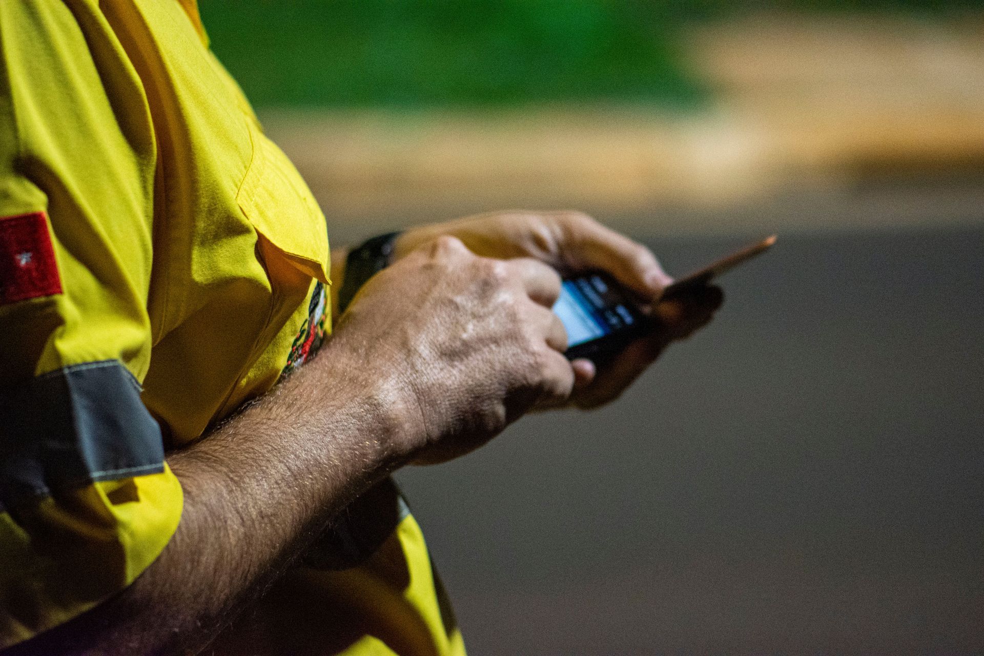 Worker in a yellow reflective shirt using a smartphone outdoors at night