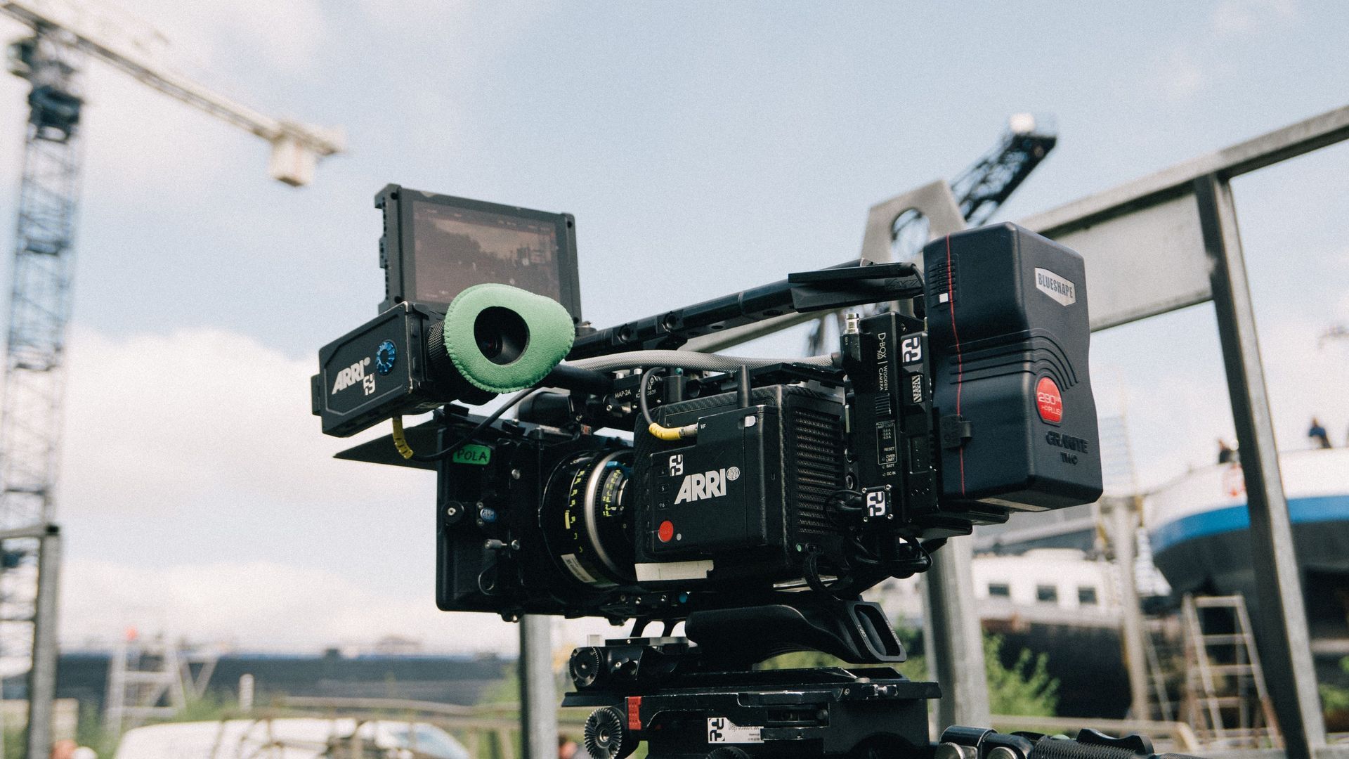 Professional video camera mounted on a tripod outdoors with buildings in the background