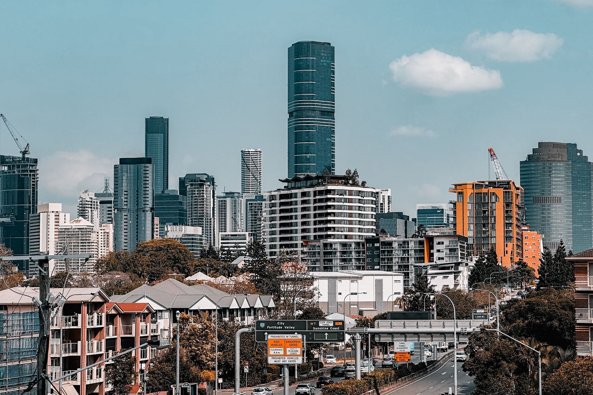 City skyline with a tall teal skyscraper above low-rise buildings under a partly cloudy sky
