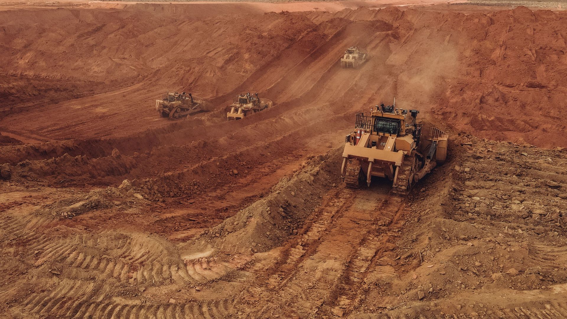 Bulldozers and dump trucks working on a dusty open-pit mine