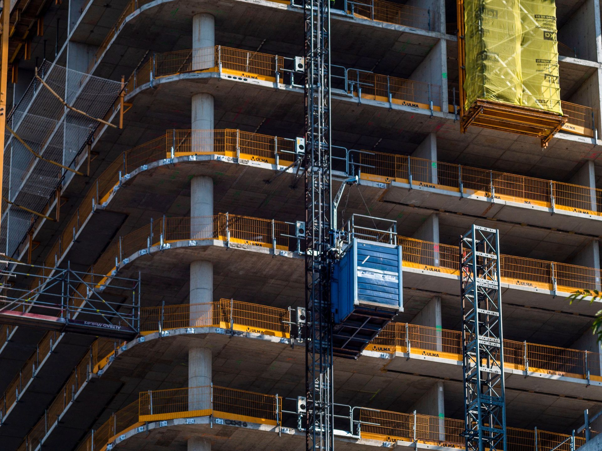 Scaffolding around a concrete building under construction, with blue lift and yellow sheeting.