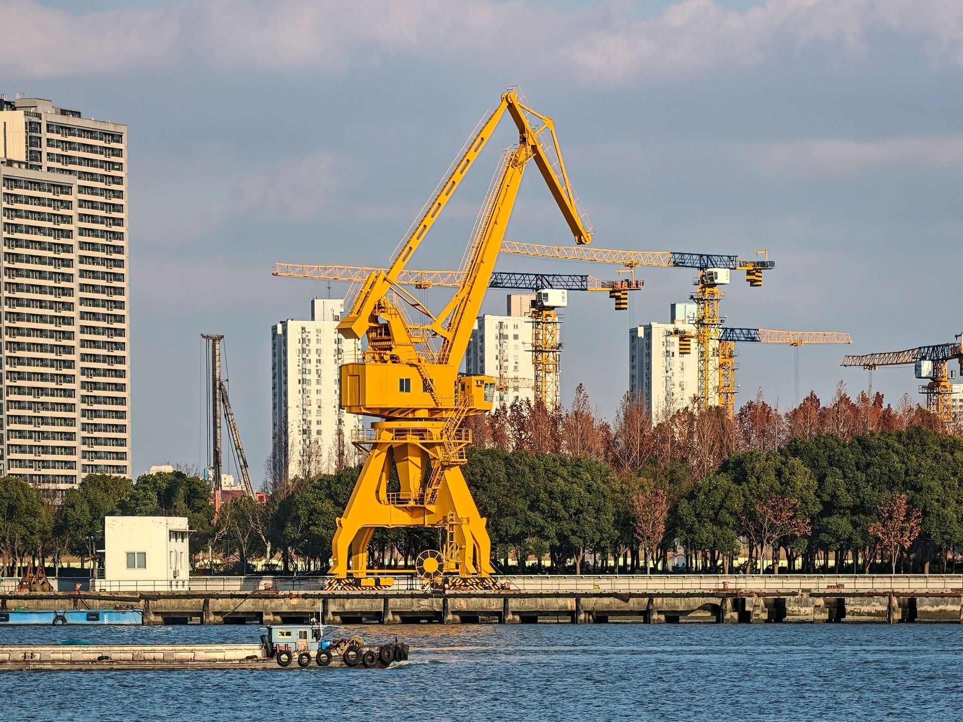 Yellow crane at a waterfront construction site with apartment buildings and trees in the background
