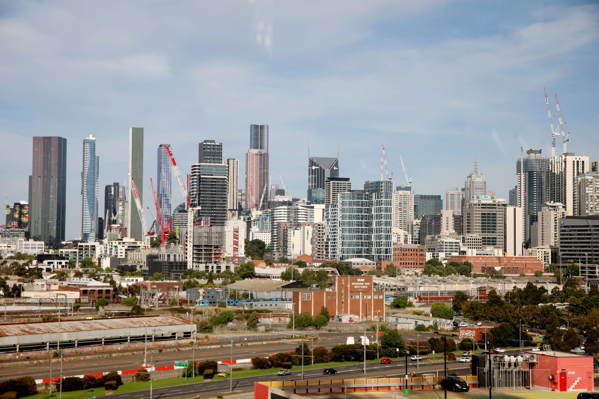 City skyline with modern high-rise buildings under a blue sky, seen above rail tracks and construction in the foreground
