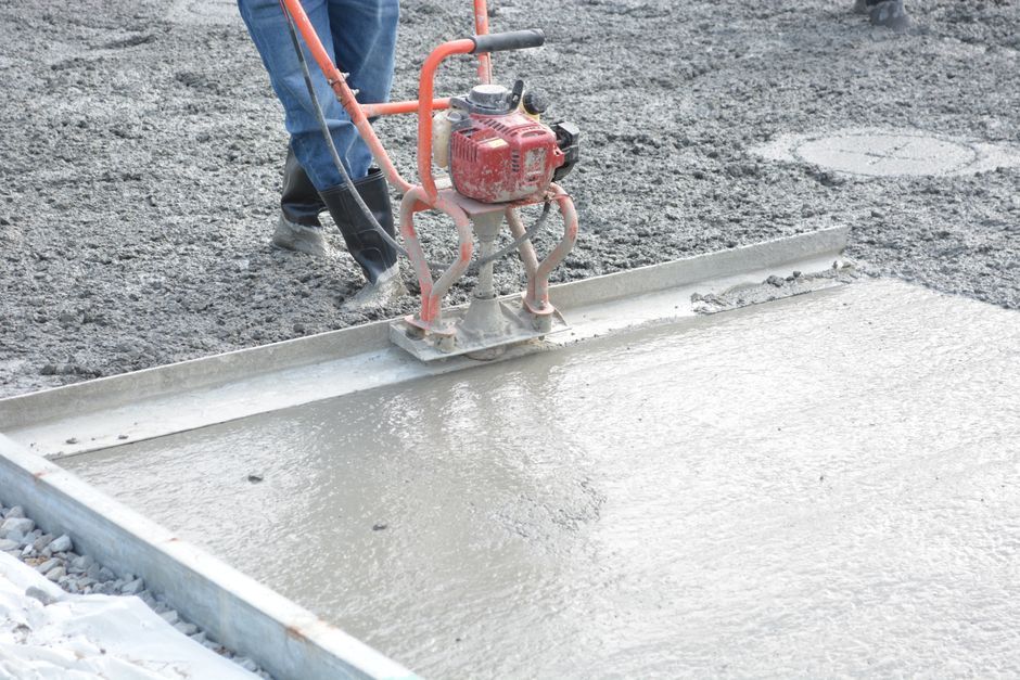 Worker using a red concrete screed to smooth wet gray concrete outdoors