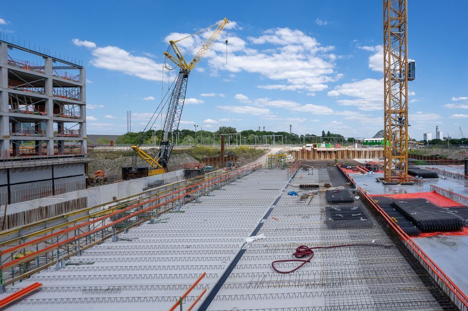 Construction site with cranes, steel framework, and concrete deck under blue sky