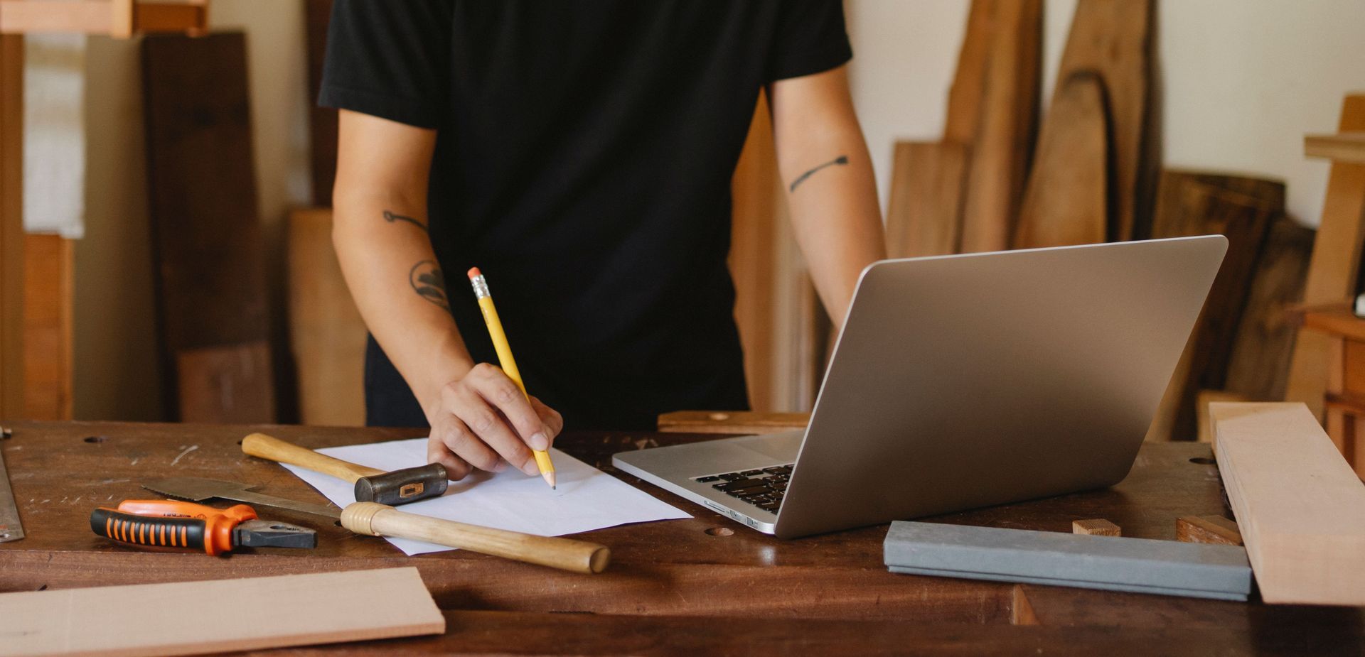 Person writing beside an open laptop at a wooden desk with a notebook and school supplies