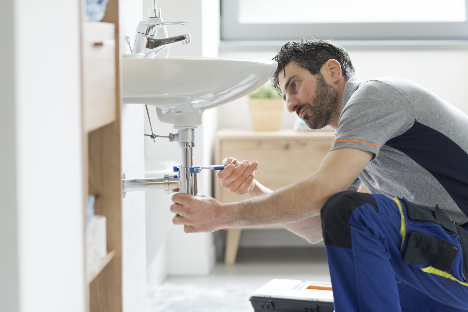 Plumber fixing a bathroom sink with tools under a white basin
