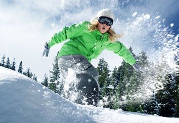 A woman in a green jacket is snowboarding down a snow covered slope.