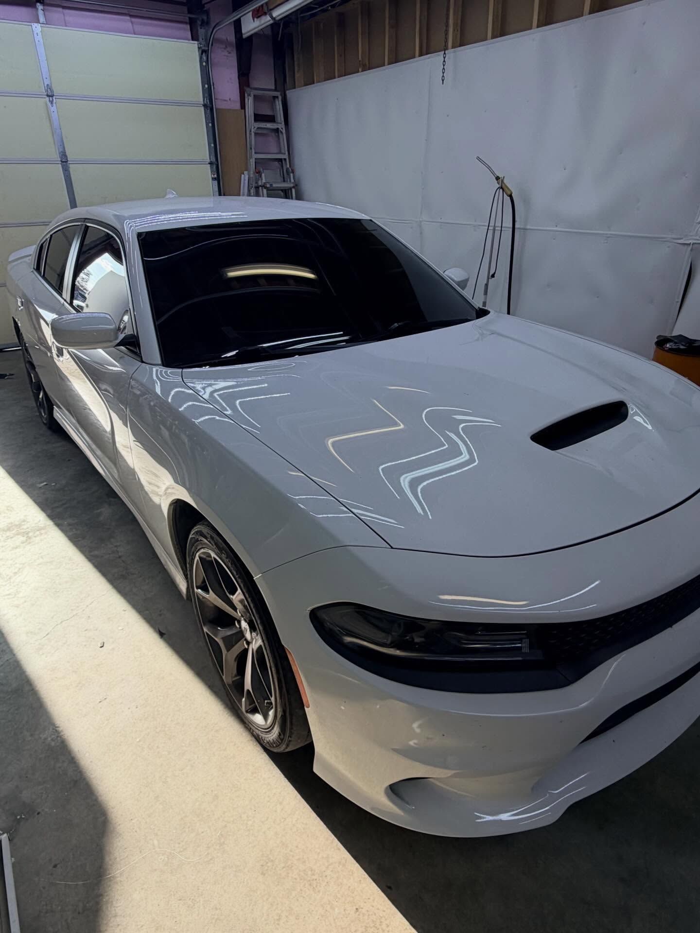 A white Dodge Charger parked indoors, angled to show its front, hood scoop, and tinted windows.
