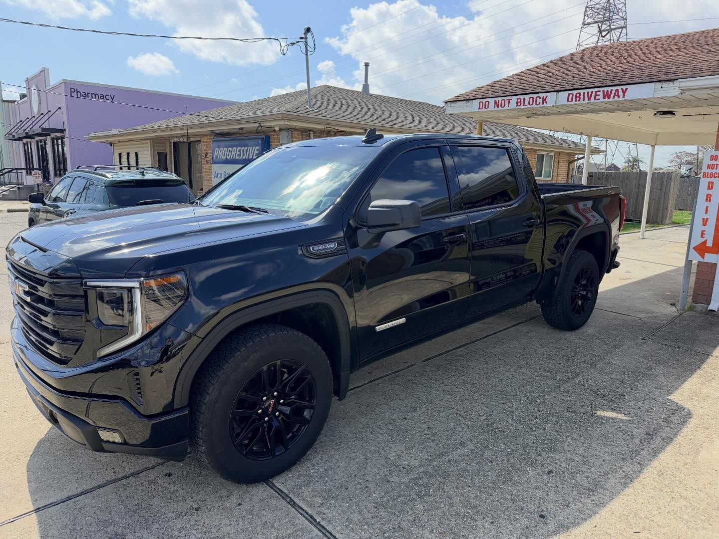A black GMC Sierra crew cab pickup truck parked at a gas station under a sunny sky.