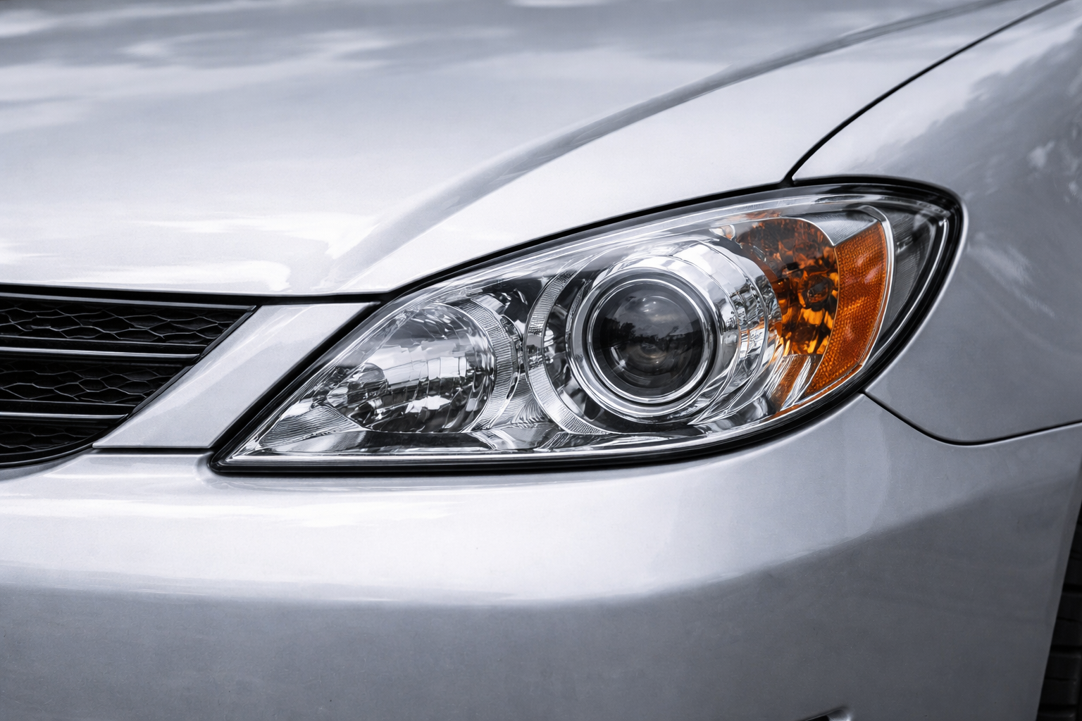 A close-up view of the silver front passenger-side headlight and hood of a modern sedan.