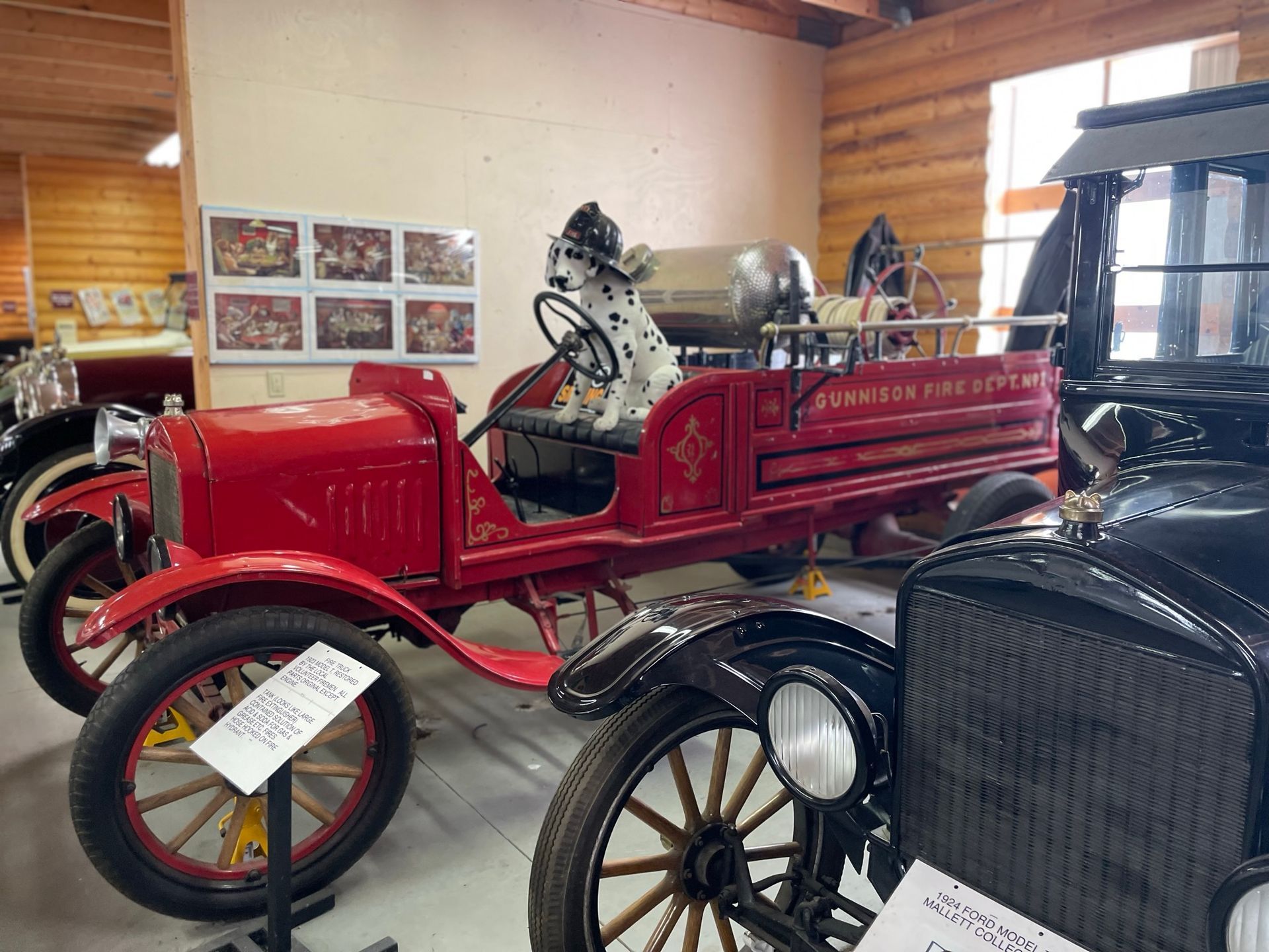 A red fire truck is parked next to a black car in a museum.