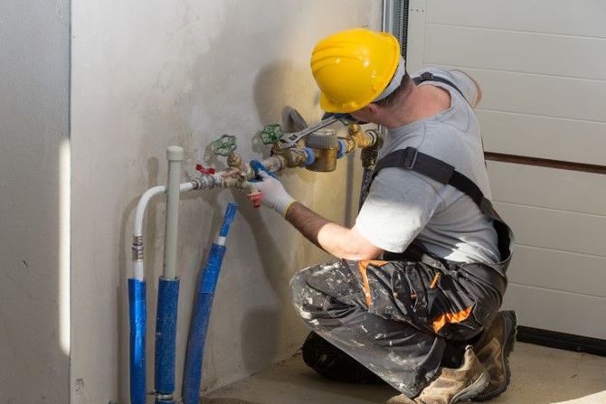Worker in a yellow hard hat repairing pipes under a sink.