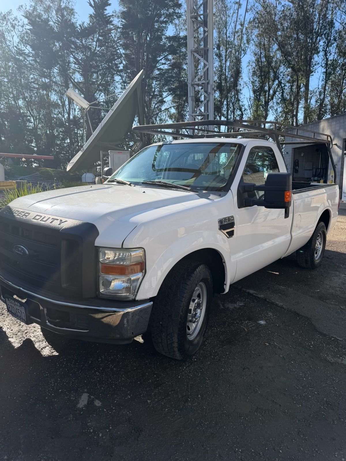 White pickup truck with open hood and damaged front bumper parked outdoors under trees