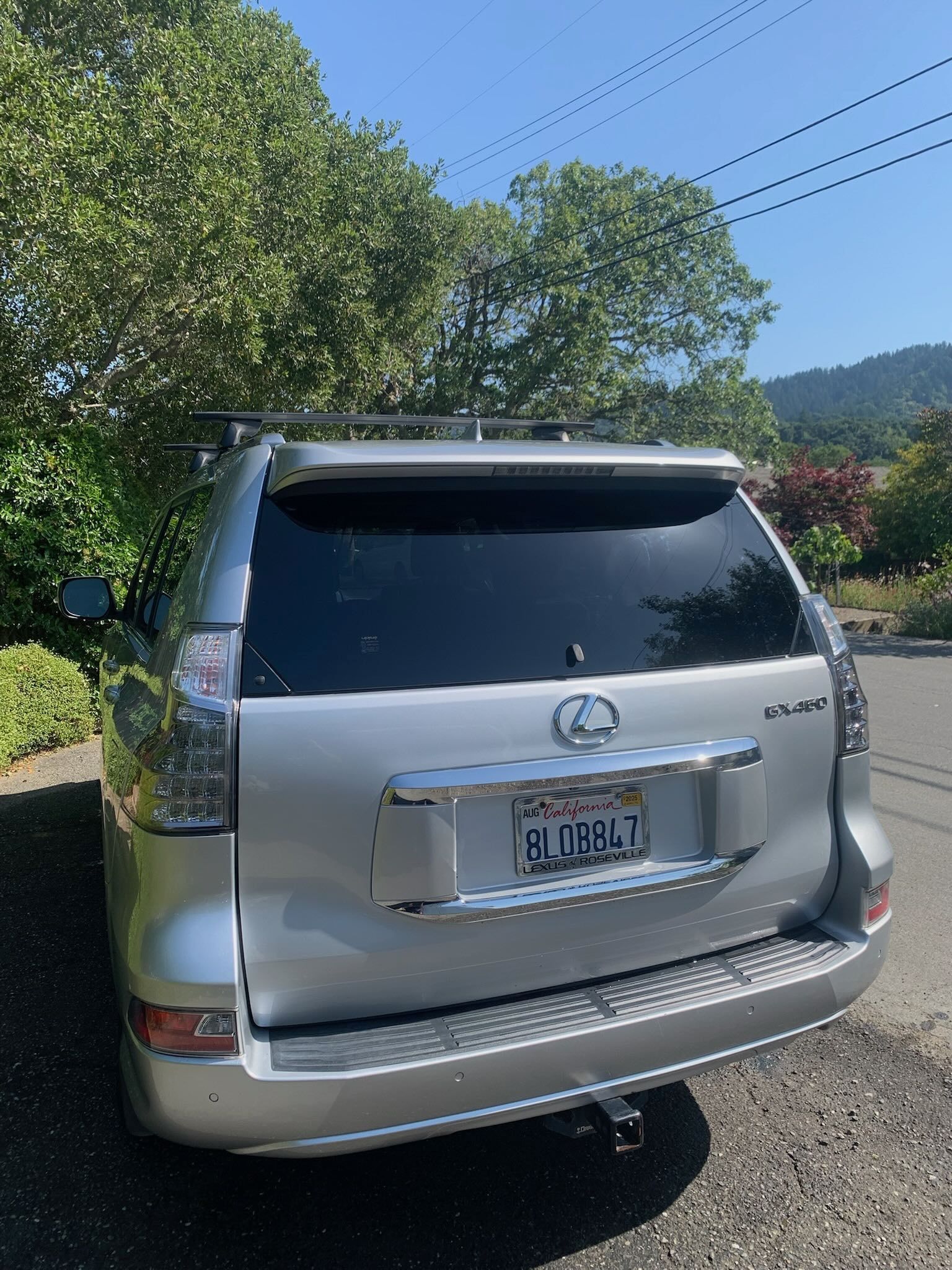 Silver Mercedes SUV parked on a sunny roadside with trees and hills in the background