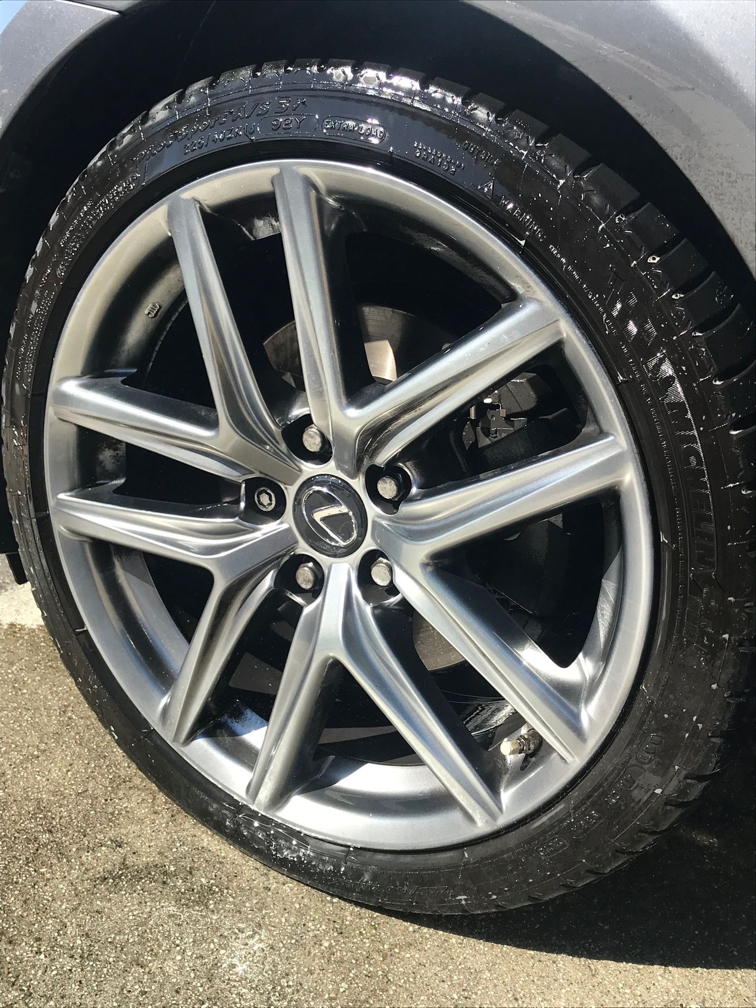 Silver alloy car wheel and tire with a Mazda logo, shown close-up on pavement.
