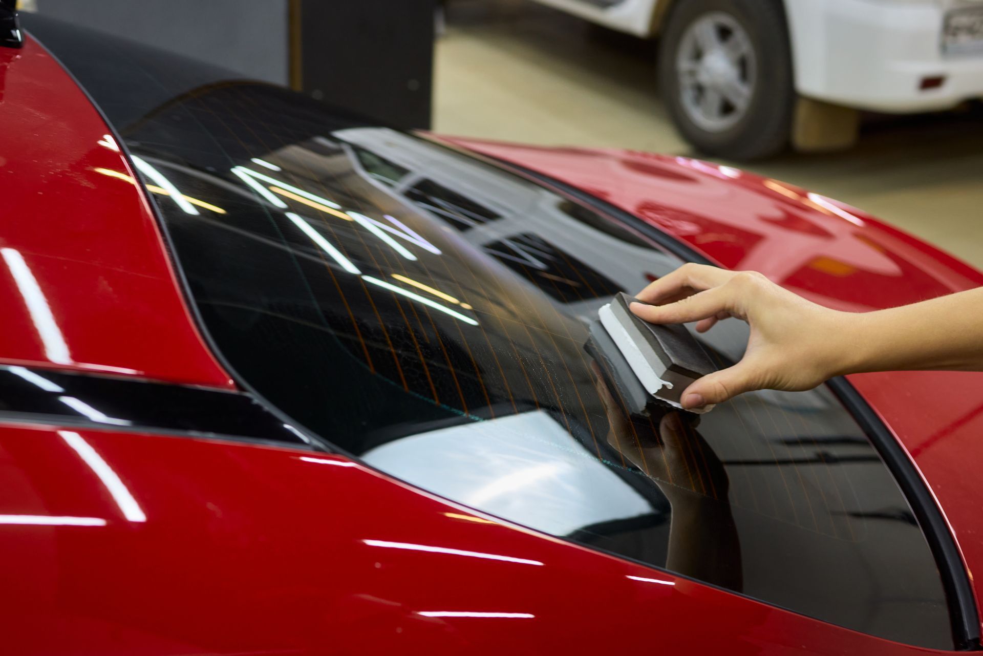 Hand wiping a red car’s windshield with a cloth in a garage