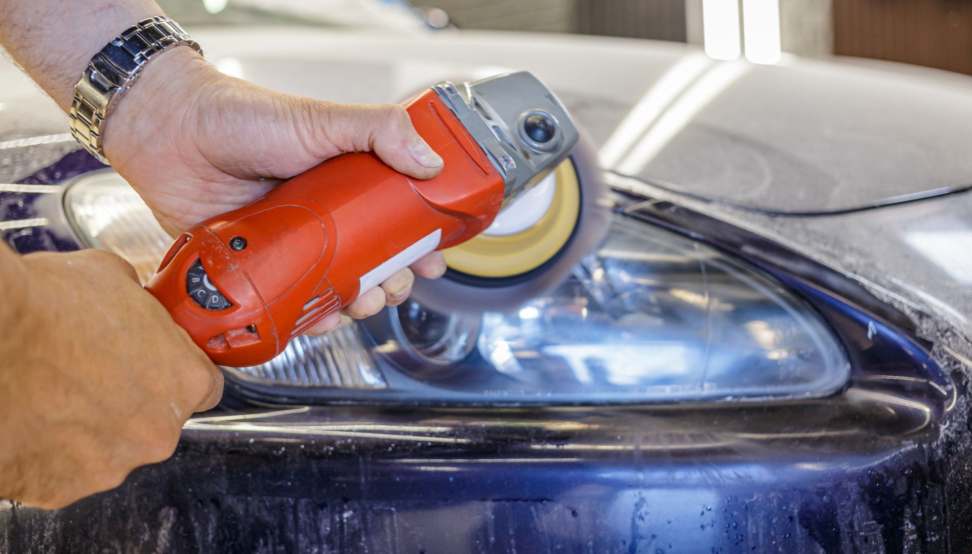 Person polishing a car headlight with an orange buffer tool