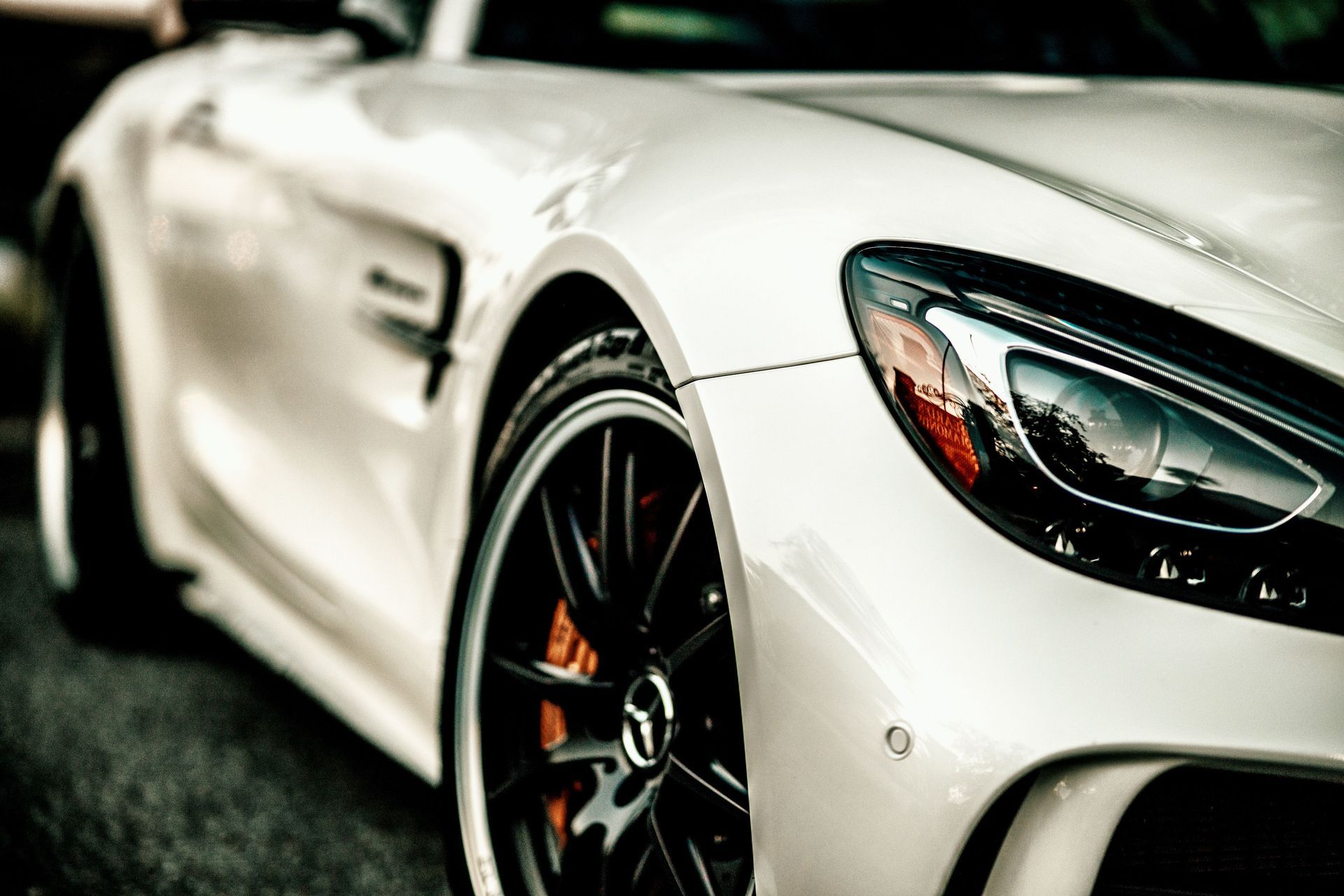 Close-up of a white sports car front wheel and headlight with sleek black trim